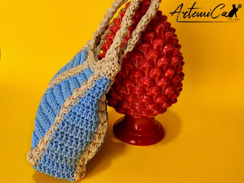 3 L'immagine mostra una borsa azzurra all'uncinetto con strisce verticali gialle, dotata di un manico coordinato e una chiusura magnetica. Sogno Mediterraneo: il fascino del mare nella tua mano.
